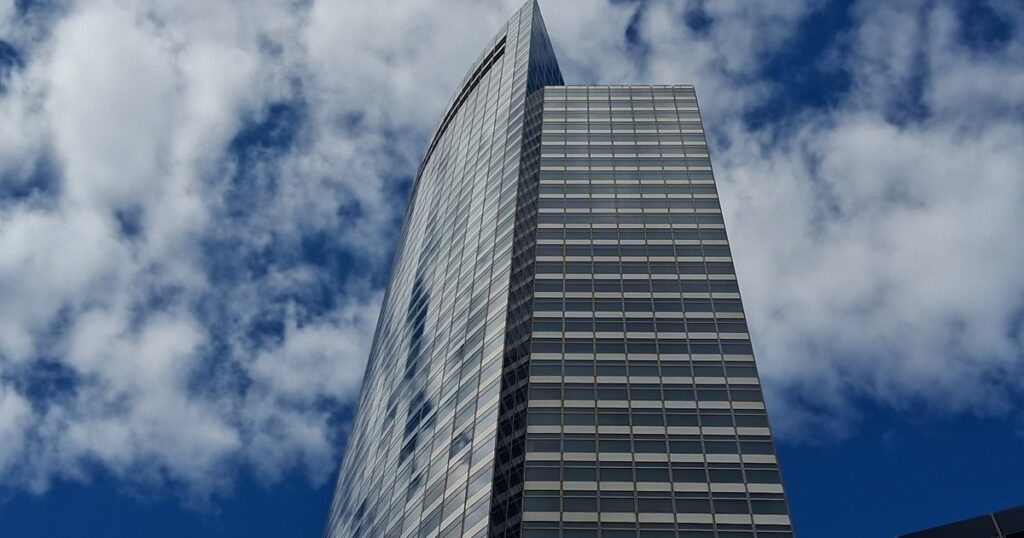 Low-angle view of 200 West Street, the Goldman Sachs headquarters tower in Lower Manhattan, against a blue sky with clouds.