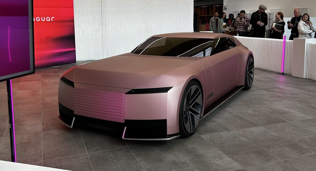 Pink Jaguar Type 00 electric concept car on display indoors as visitors look on