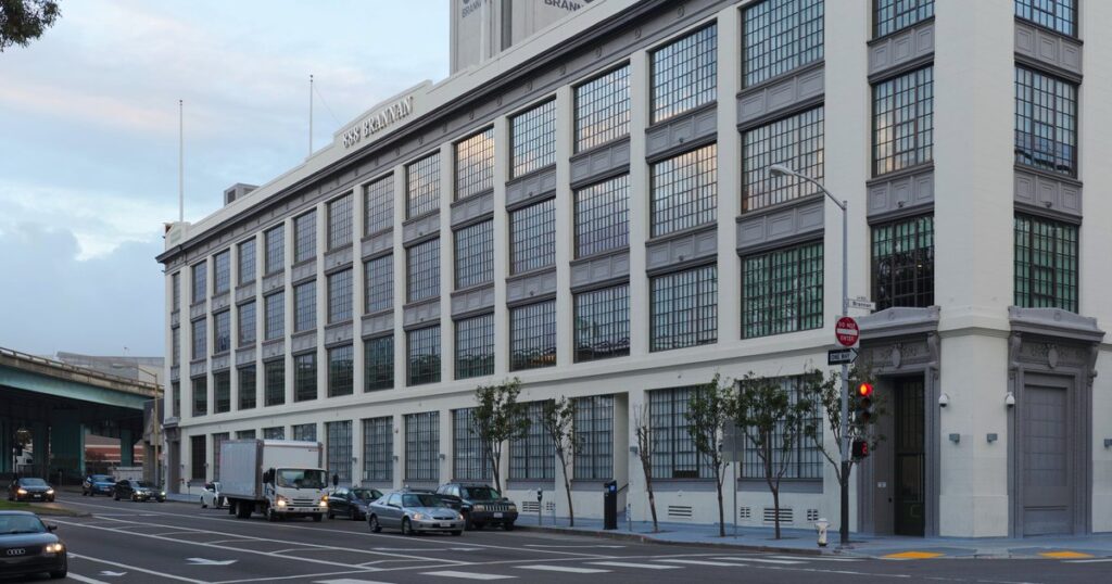 888 Brannan Street in San Francisco, the building that houses Airbnb's headquarters: a long white industrial-style building with rows of large gridded windows at dusk, with cars on the street in front.